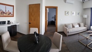 A modern hotel room with a dining area, a sofa, a TV, and a kitchen area with a microwave and refrigerator. - Hotel Plaza Matamoros (Matamoros)