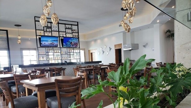 A restaurant with wooden tables and chairs, a bar area with shelves of bottles, and hanging pendant lights. - Hotel Plaza Matamoros (Matamoros)