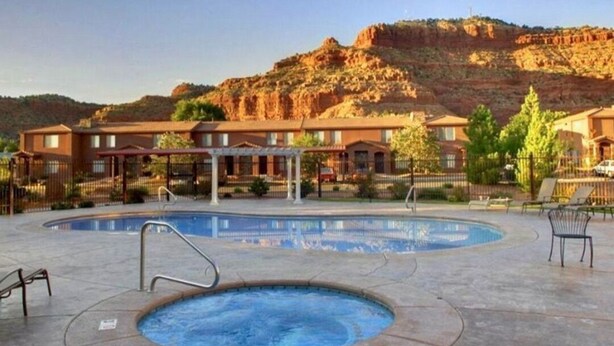 A hotel with a swimming pool, outdoor seating, and a mountainous backdrop. - The Happy Cactus Home (Kanab)
