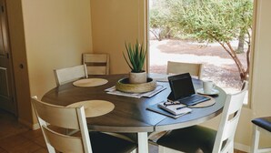 A round dining table with a laptop, notebook, and pen, surrounded by white chairs. - The Happy Cactus Home (Kanab)