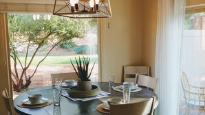 A dining area with a round table, chairs, a hanging light fixture, and a view of the outdoors. - The Happy Cactus Home (Kanab)