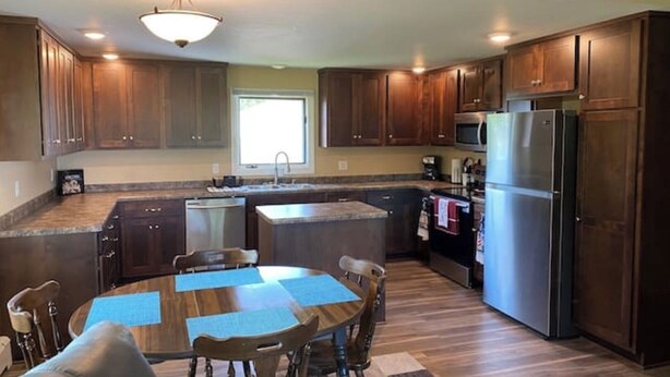 A modern kitchen with wooden cabinets, a stainless steel refrigerator, a built-in oven, and a dining area with a round table and chairs.