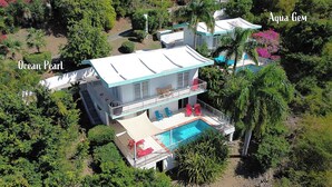 Une maison à deux étages avec une piscine, entourée d’une végétation luxuriante.