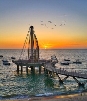 Uma ponte com uma torre central, rodeada por água e barcos, durante o pôr do sol.