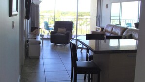 Ein geräumiger Wohnbereich mit Deckenventilator, Esstisch und Sofa. Ein großes Fenster bietet einen Blick ins Freie.