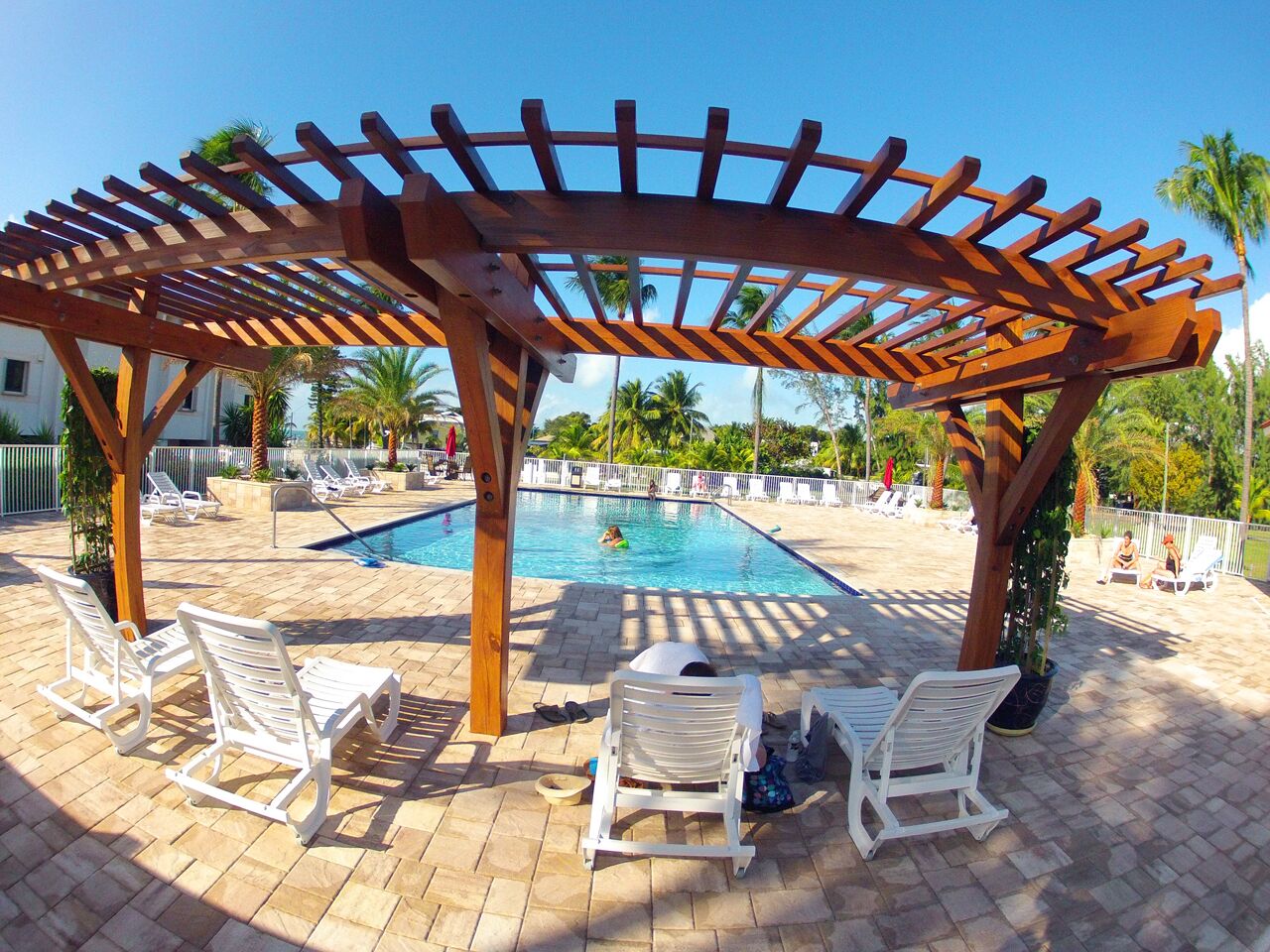 A pool area with a wooden pergola, lounge chairs, and a swimming pool.
