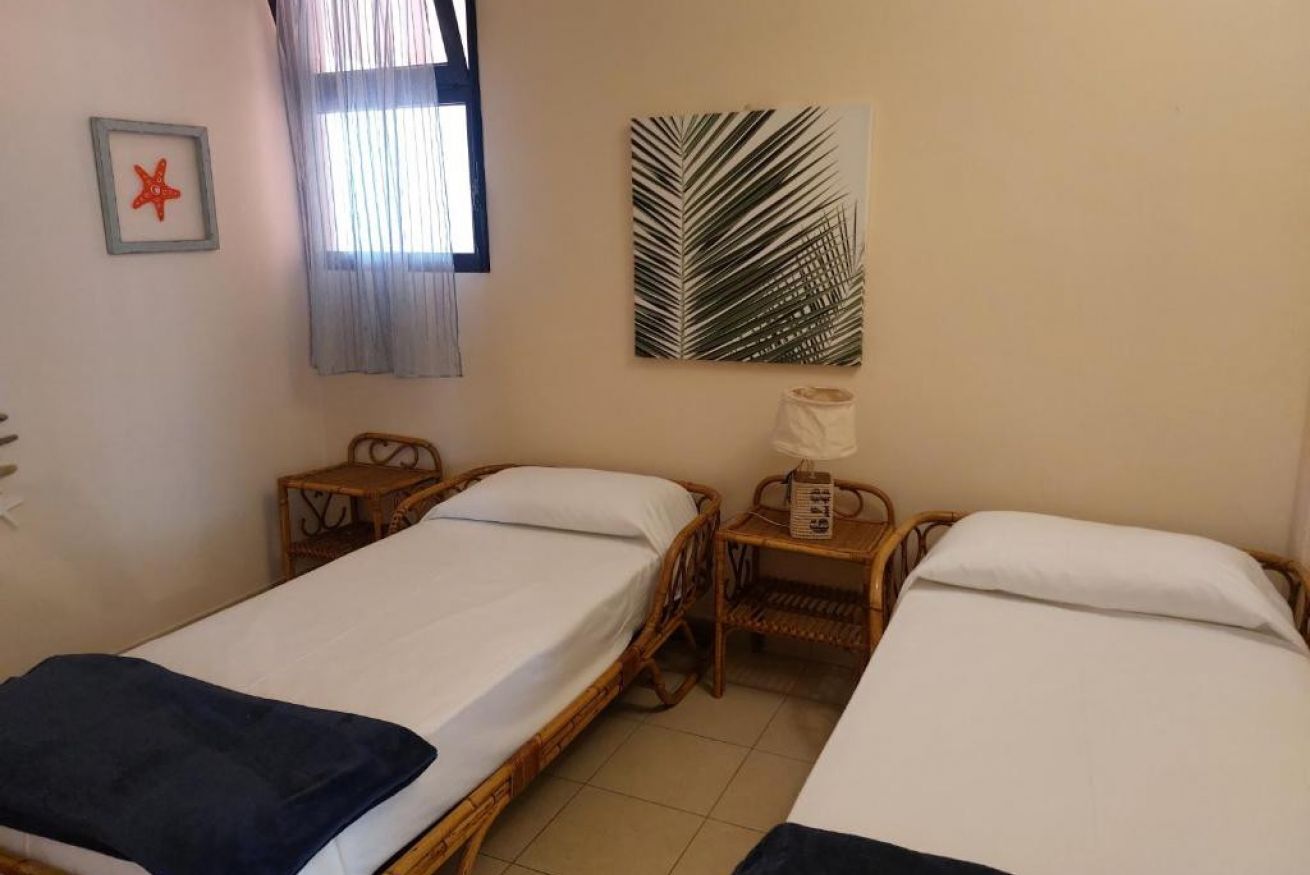 A room with two single beds, a small table with a lamp, a framed picture, and a large leaf-patterned artwork on the wall.