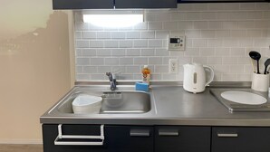 A modern kitchen with a stainless steel sink, a kettle, and a coffee maker. There is a white tiled backsplash and a black cabinet above the sink. - sincereresidence (Osaka)
