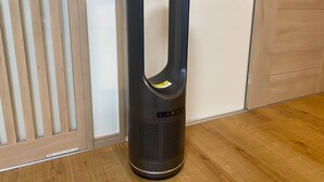 A black portable air purifier with a handle, placed on a wooden floor next to a white wall and a wooden door. - sincereresidence (Osaka)