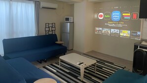 A modern living room with a blue sofa, a small table, and a wall-mounted TV displaying streaming services. - sincereresidence (Osaka)