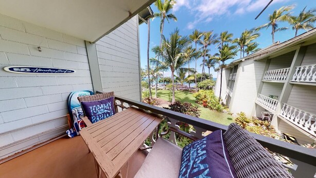 A balcony with a wooden table and two chairs, a surfboard, and a sign on the wall.