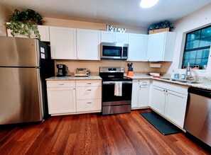 Una cocina con armarios blancos, un refrigerador de acero inoxidable, un microondas, un tostador y una cafetera.