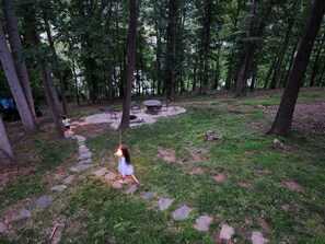 A forested area with a stone pathway leading to a seating area with a table and chairs.