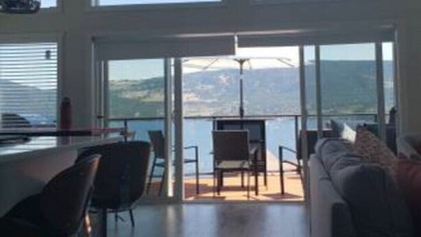 A spacious living area with a high ceiling and large windows offering a view of the outdoors.