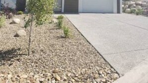 A two-story house with a garage, a small garden with gravel and plants, and a clear sky.