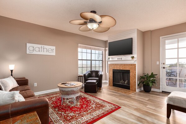 A living room with a fireplace, a television mounted above it, and a large window. - Skyline View, City & Mountain Views, Golf nearby, bicycling, swimming pool (Tucson)