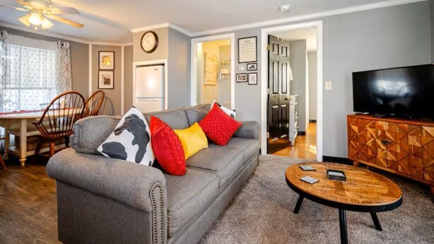 A living room with a grey sofa, red and yellow cushions, a wooden coffee table, and a TV on a wooden cabinet. - Newly Remodeled 1-BR Close to Everything yet Very Private (Wallingford)