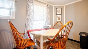 A dining area with a round table, four wooden chairs, a white tablecloth, a basket, and a black trash bin. - Newly Remodeled 1-BR Close to Everything yet Very Private (Wallingford)