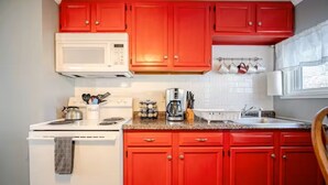 A kitchen with red cabinets, a white stove, a microwave, and a coffee maker. - Newly Remodeled 1-BR Close to Everything yet Very Private (Wallingford)