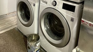 A stack of two LG washing machines with a metal container on the floor.