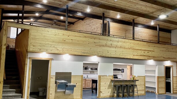 A spacious indoor area with a high ceiling, wooden beams, and a mezzanine level.