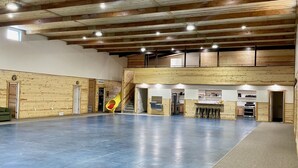 A spacious indoor area with a high ceiling, wooden beams, a central slide, and a kitchen area.