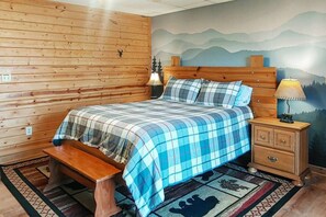 Een kamer met houten lambrisering, een bed, een bankje, nachtkastje en een muurschildering.