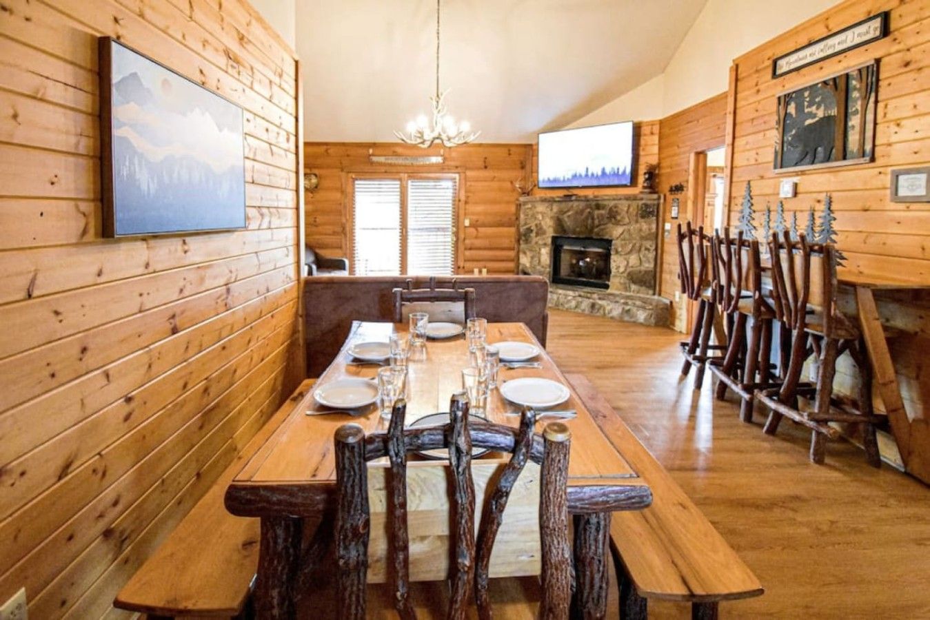 Un interior de madera con una mesa de comedor lista para cuatro comensales, una chimenea y un televisor montado en la pared.