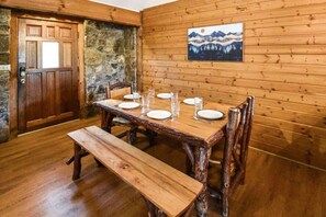 A wooden dining table with benches, a stone wall, and a painting on the wall.