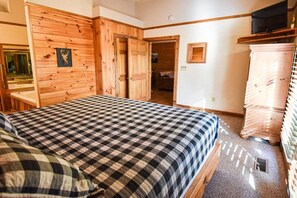 Une chambre avec une couvre-lit à carreaux, des murs en bois, une télévision et une armoire.