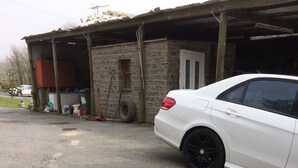 A lamb standing on a gravel driveway in front of a white car and a building with a garage. - The Canteen Beautiful 1-bed Apartment in Keswick (Keswick)