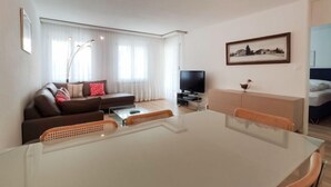 Un salon moderne avec une table à manger blanche, un canapé marron et un téléviseur à écran plat.