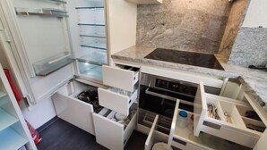 Une cuisine compacte dotée d’appareils électroménagers intégrés, notamment une cuisinière, un four et un réfrigérateur à plusieurs étagères.