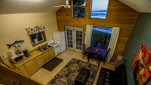 A compact kitchen with a microwave, stove, and refrigerator. There is a dining area with a table and chairs, and a large window overlooking a scenic view. -  'Chisik Cabin'  Waterfront/Sunset Views (Kasilof)