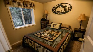 Une chambre à coucher avec un lit, une fenêtre, une lampe, une commode et un élément décoratif mural.