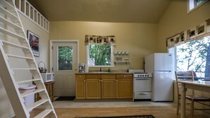 Une cuisine avec des meubles en bois, une cuisinière, un réfrigérateur, un four à micro-ondes et une fenêtre donnant sur des arbres.