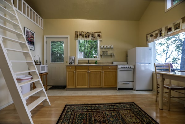 Una cucina con mobili in legno, un fornello, un frigorifero, un forno a microonde e una finestra vista alberi.