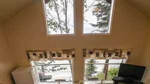 Il s’agit d’un espace de vie compact comprenant une cuisine, un coin repas et un coin salon. Il est doté d’une grande fenêtre offrant une vue sur les arbres, d’une cheminée et d’un téléviseur.