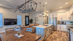 A modern kitchen with a central island, stainless steel appliances, and a dining area with a wooden table and chairs. - ADOBE MANOR // Main + Guest Home // Sleeps 20 (Mesa)