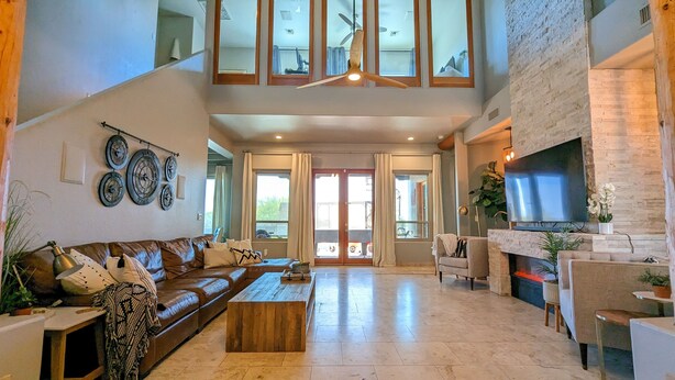 A spacious living room with a leather sofa, wooden coffee table, and a flat-screen TV mounted on a brick wall. - A D O B E  -  E S T A T E (Mesa)