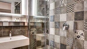 A modern bathroom with a white sink, glass shower enclosure, and patterned tiles.