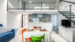 A modern apartment with a dining area, kitchen, and a loft bedroom.