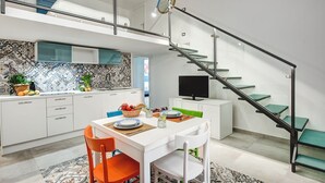A modern kitchen with white cabinets, a glass staircase, and a dining area with a white table and orange chairs.