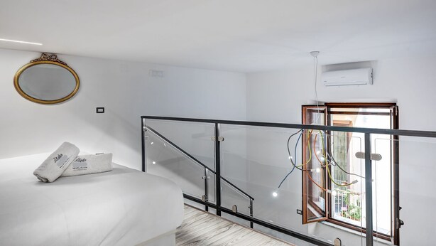 A modern bedroom with a bed, a round mirror, and a glass railing overlooking a balcony.