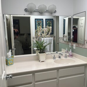 A bathroom with a large mirror, two sinks, a potted plant, and decorative wall art.