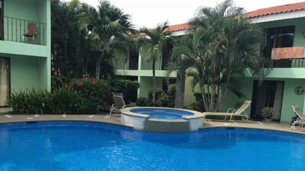 A swimming pool with lounge chairs and a hot tub, surrounded by greenery and a building with a red-tiled roof. - Villa Riviera (Sardinal)