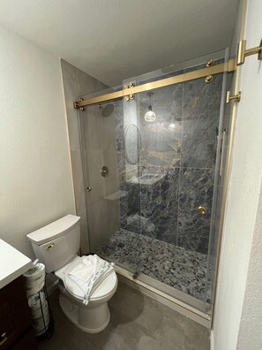 A modern bathroom with a glass-enclosed shower, a toilet, and a marble backsplash. - 209A Beach Living at its Best (Oceanside)