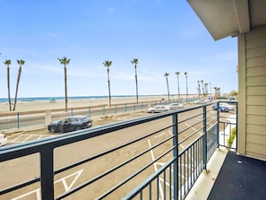Un balcon avec vue sur une plage, des palmiers et des voitures garées.