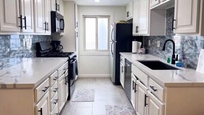 A modern kitchen with white cabinetry, a black refrigerator, a stove, and a sink.