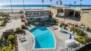 A pool area with a clear view of the ocean, a building with a patio, and palm trees.